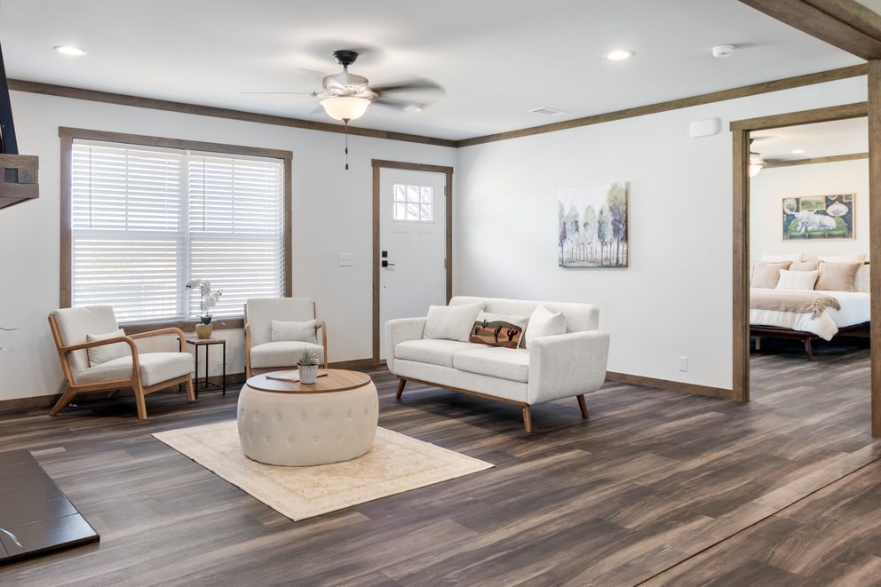 Bright bedroom sitting area with white sofa, chairs, round ottoman, and doorway to a bed area