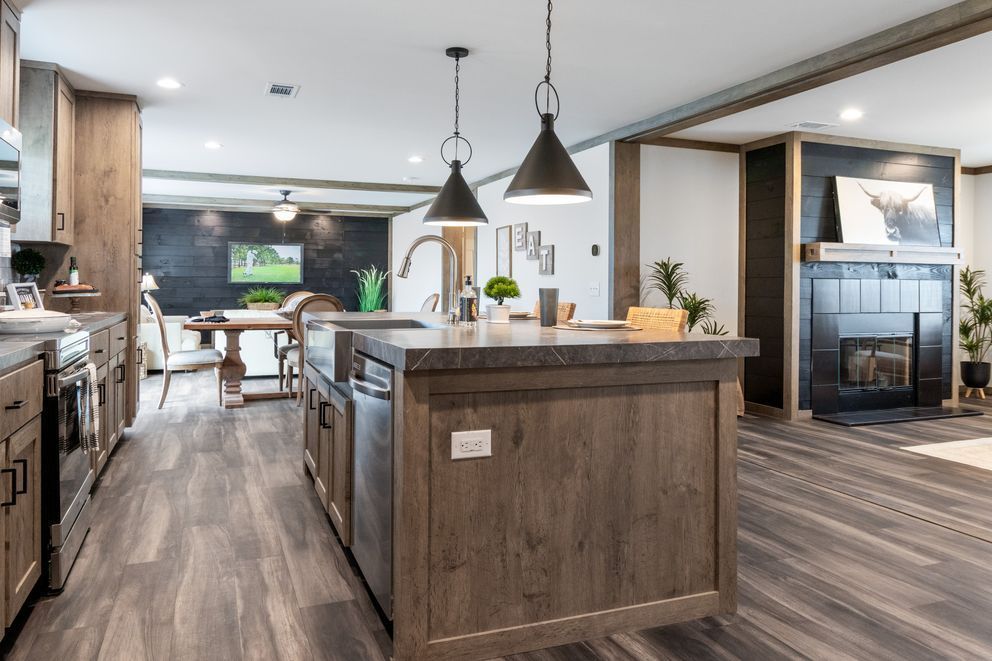 Modern open kitchen with wood cabinets, island, pendant lights, and large windows overlooking a dining area