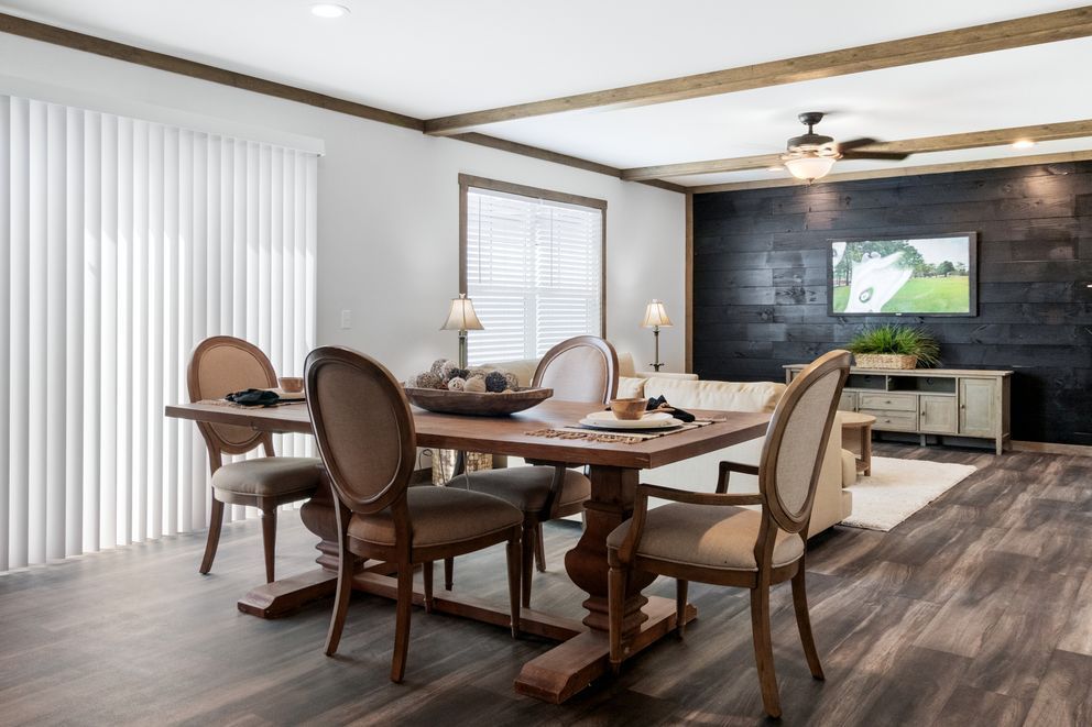 Modern dining room with wooden table, upholstered chairs, large windows, and a TV on a dark accent wall