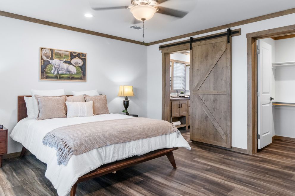 Bright bedroom with a bed, barn-style sliding door, ceiling fan, and bedside lamp