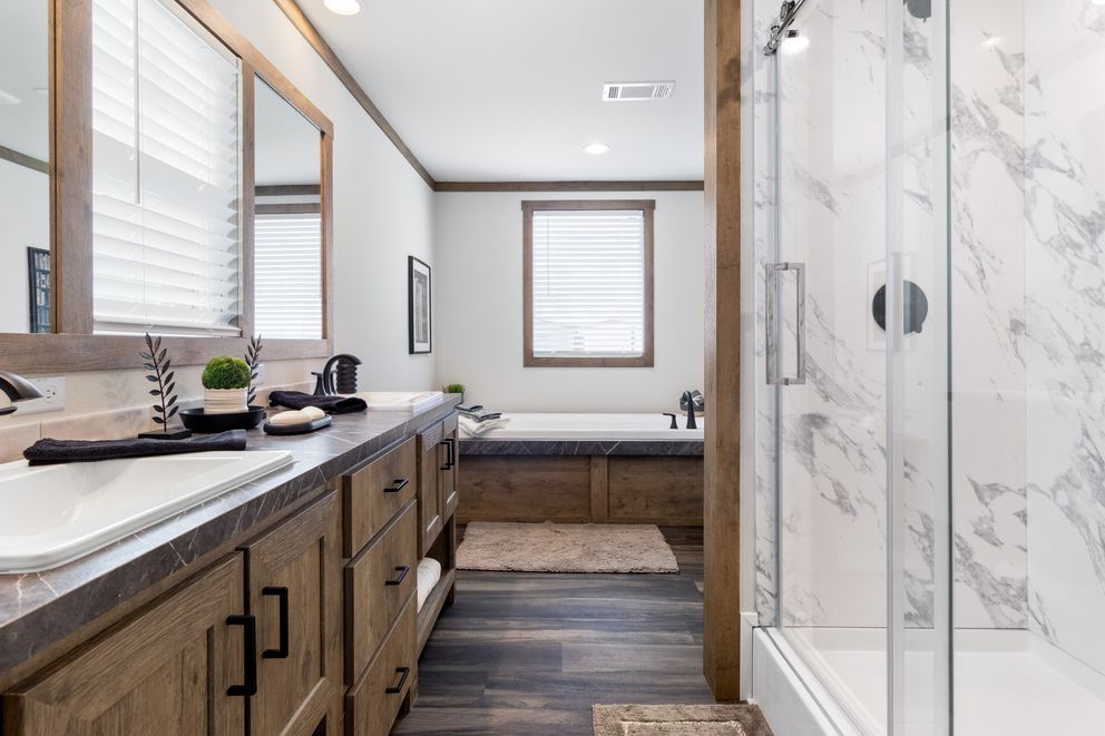 Modern bathroom with double vanity, large mirror, glass shower, and window-lit neutral decor