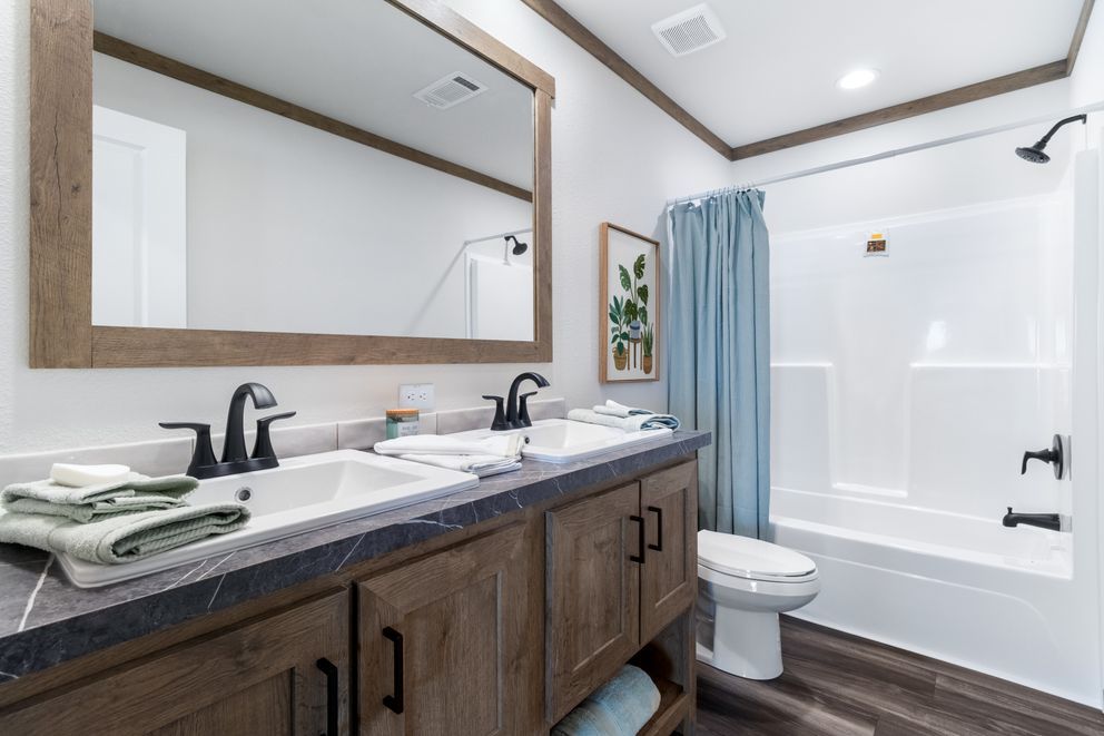 Modern bathroom with double vanity, large mirror, white tub, and blue shower curtain