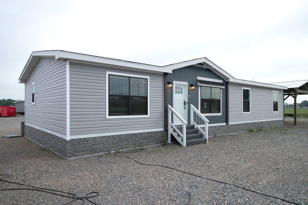 Gray single-story modular home with a small front porch and steps on a gravel lot