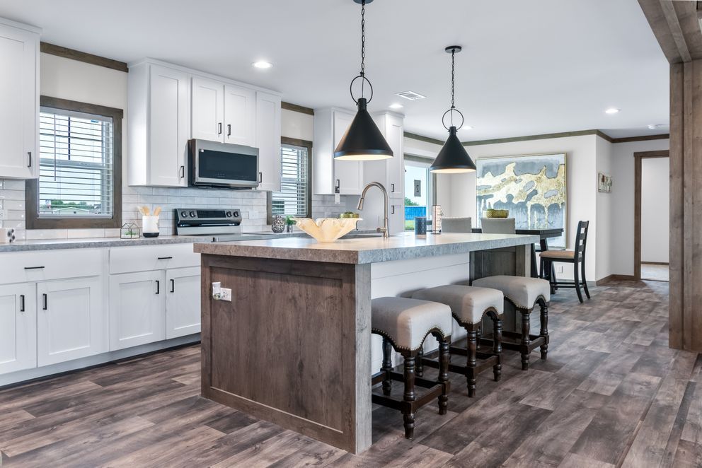 Modern kitchen with white cabinets, dark island, barstools, pendant lights, and open dining area