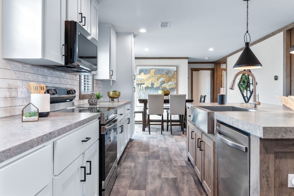 Bright modern kitchen opening to dining area with white cabinets, gray counters, and pendant lights