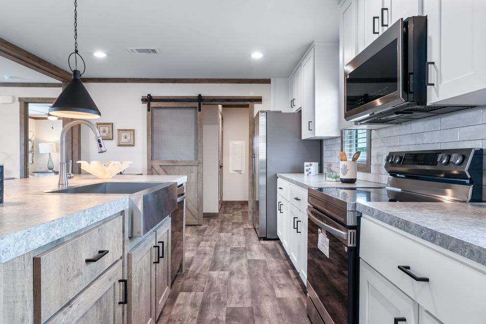 Modern kitchen with island, white cabinets, wood floors, stainless appliances, and a hanging pendant light