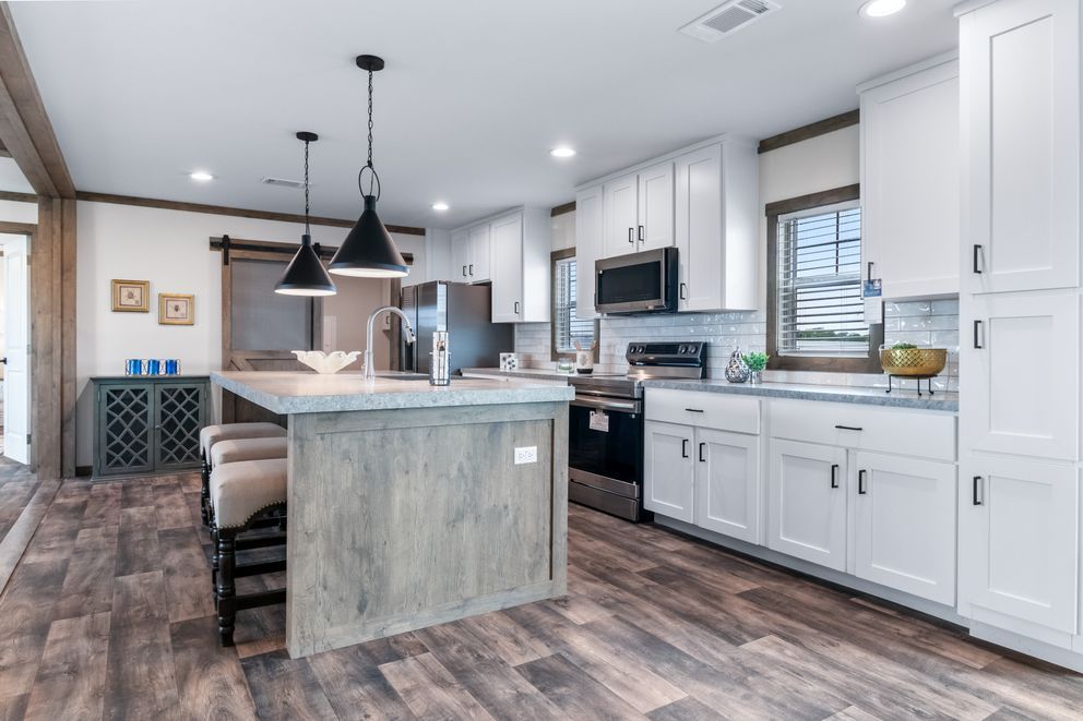 Modern kitchen with gray island, white cabinets, pendant lights, and wood-look flooring