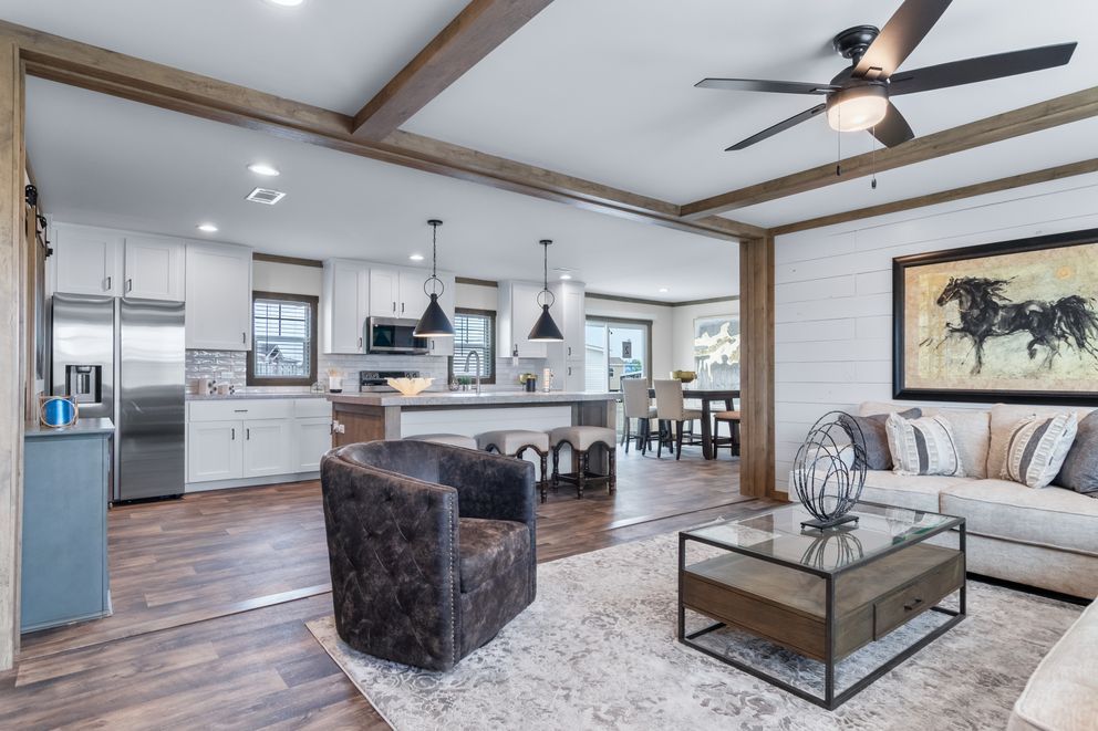 Open-concept living room and kitchen with gray sofas, dark wood floors, and ceiling fan