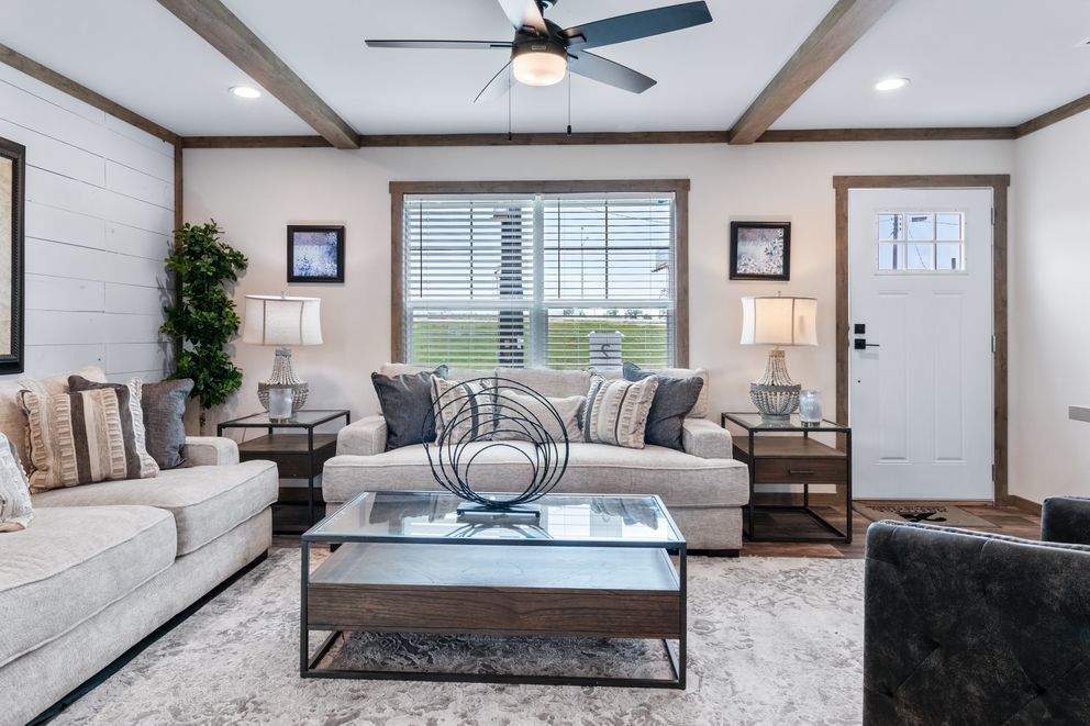 Bright living room with beige sofa, coffee table, wall art, ceiling fan, and front door.