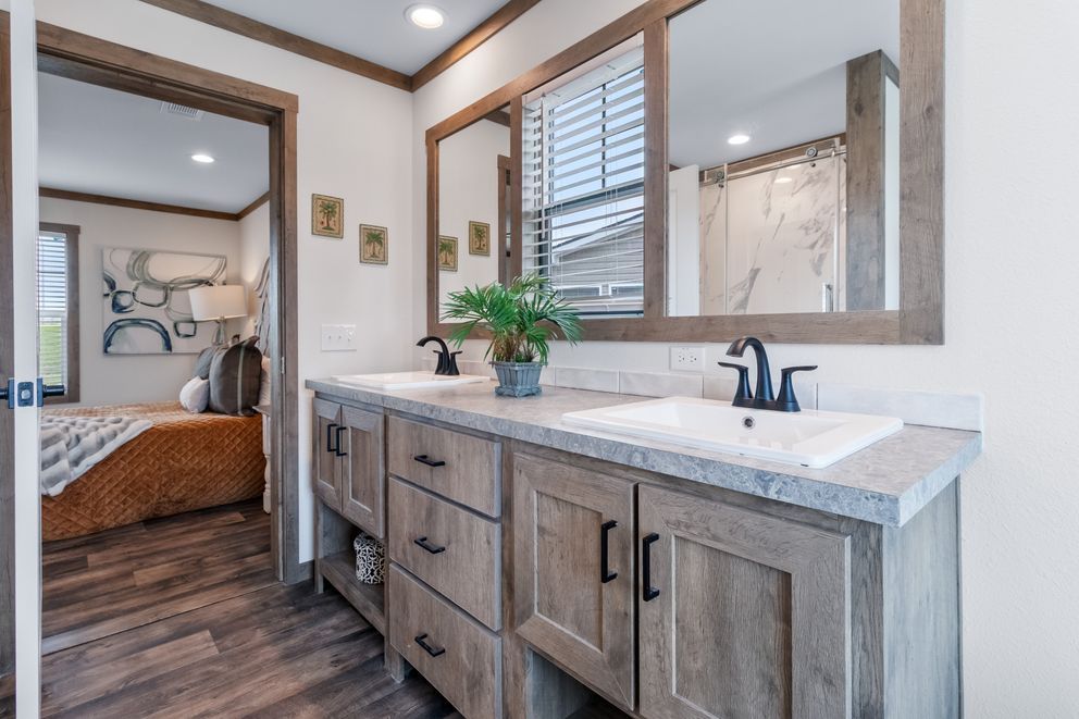 Modern bathroom vanity with double sinks, wood cabinets, and large mirror in a bright bedroom suite