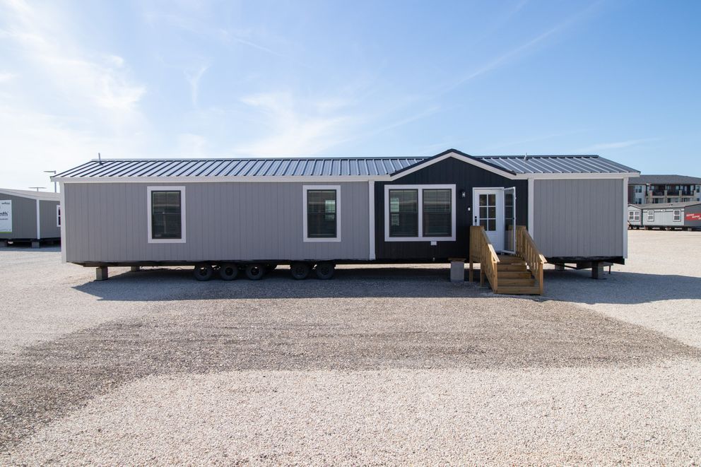 Portable gray modular building with front steps on a gravel lot under a blue sky