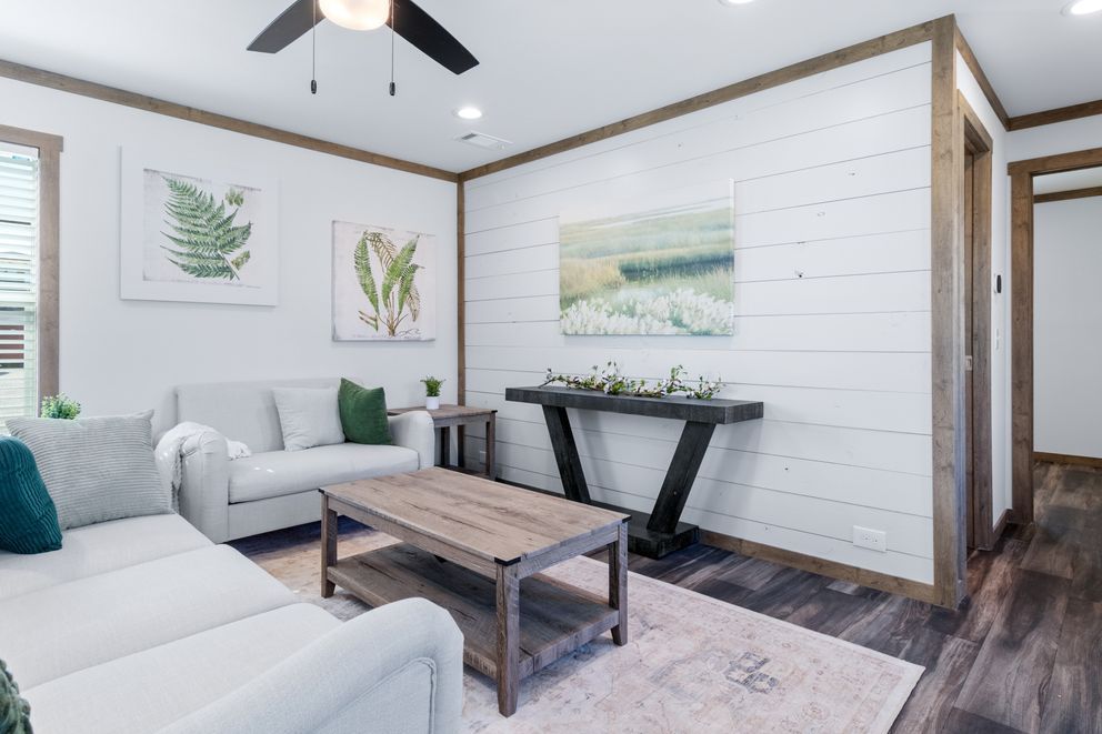 Bright living room with white sofa, coffee table, wall art, and a black standing desk by a shiplap wall.