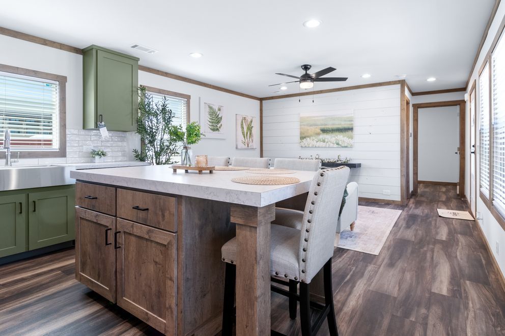 Bright modern kitchen and dining area with green cabinets, wood island, and white upholstered chairs.