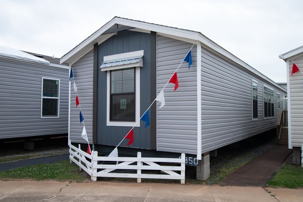 Small gray mobile home with red and blue bunting and a white fence in front
