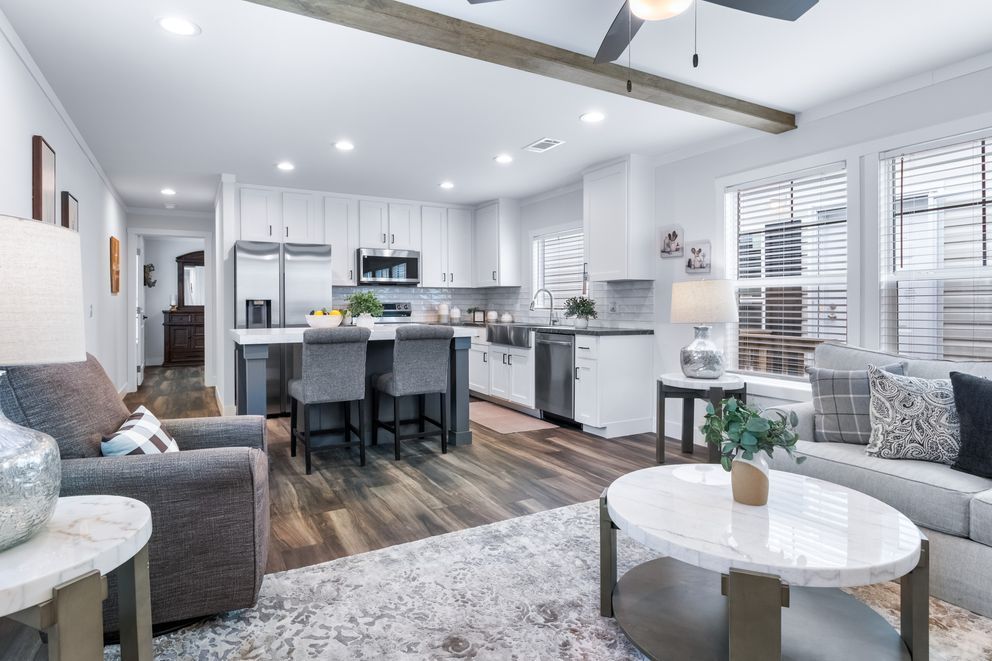 Bright open-concept living room and kitchen with gray furniture, white cabinets, and wood floors