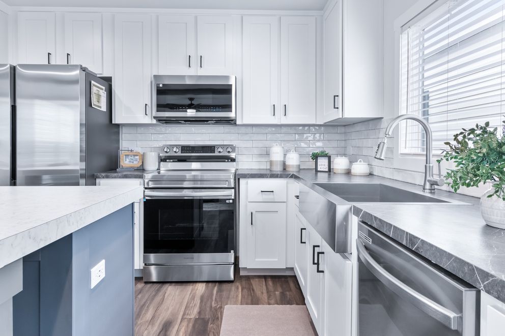 Bright modern kitchen with white cabinets, stainless appliances, gray counters, and wood flooring