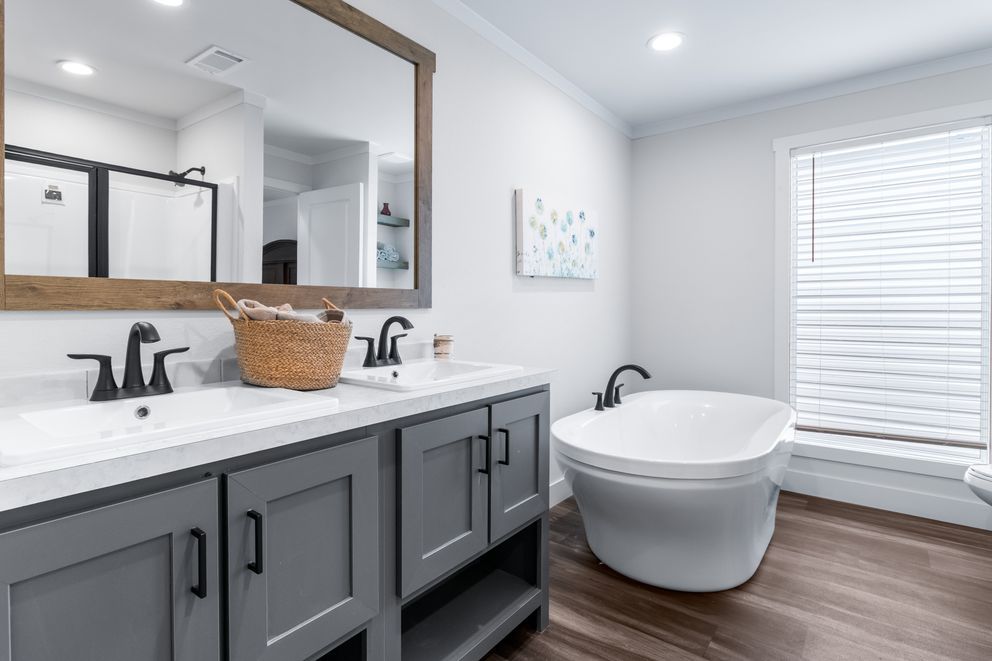 Modern bathroom with double vanity, large mirror, freestanding tub, and window blinds in gray and white tones