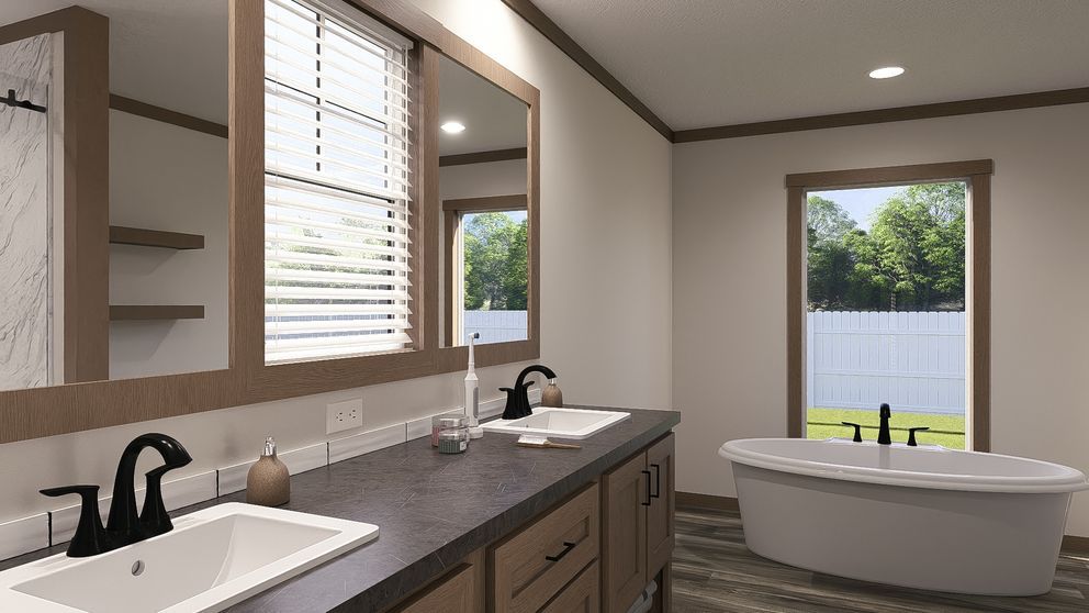 Bright bathroom with double vanity, large mirror, freestanding tub, and window overlooking trees