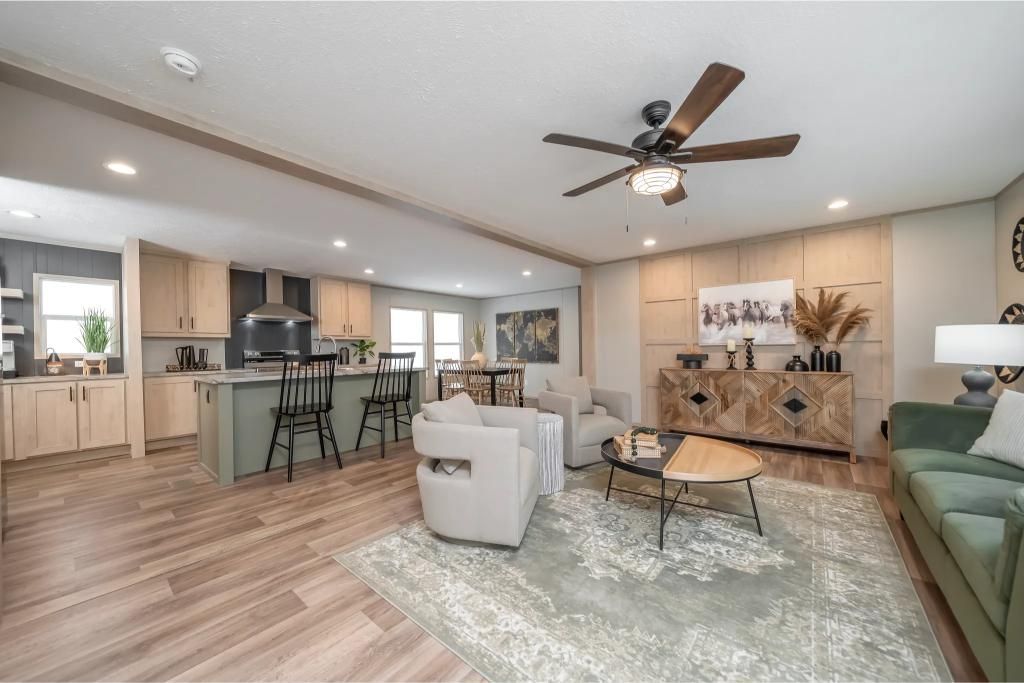 Spacious modern living room with kitchen, wood floors, green sofa, white chairs, and ceiling fan