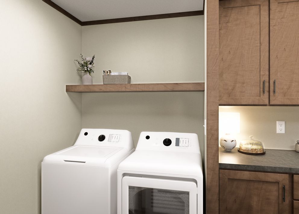 Laundry room with two white washer and dryer units, wood shelf, and adjacent kitchen cabinets
