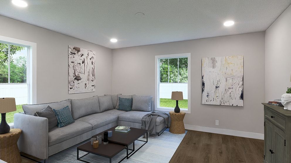 Bright living room with gray sectional, coffee table, artwork, windows, and wood floors