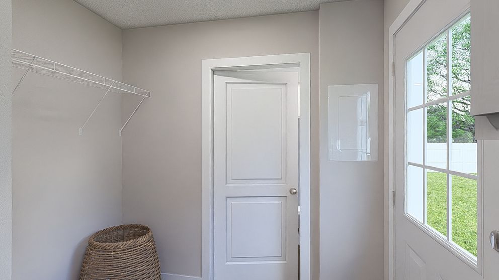 Bright empty laundry room with white door, wire shelf, basket, and window overlooking greenery