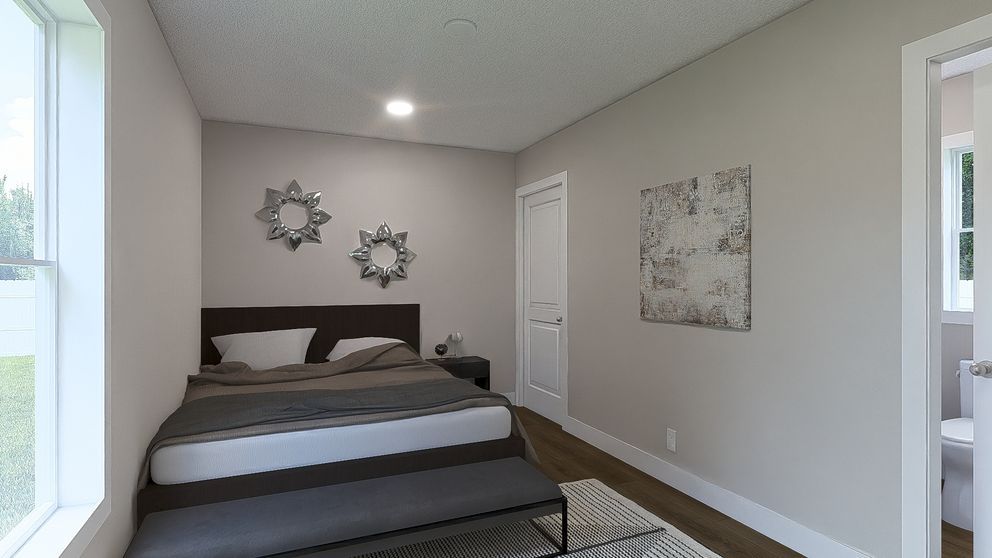 Small bedroom with a dark bed, beige walls, wall art, and a window letting in daylight.