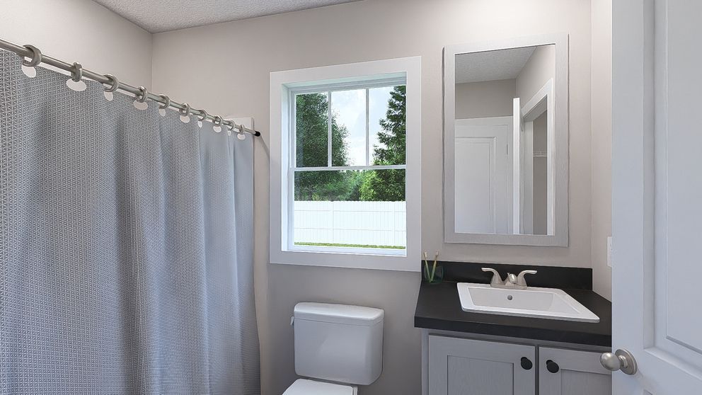 Small bathroom with gray shower curtain, toilet, vanity, mirror, and a window.