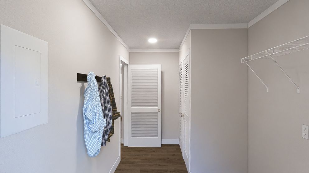 Narrow hallway with white walls, hanging clothes, and a closed white door at the end