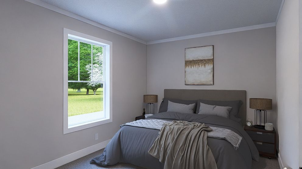 A neatly made bedroom with a gray bed, bedside lamps, and a window overlooking greenery.