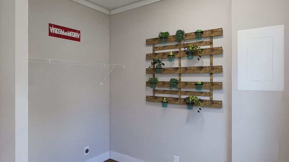 Empty beige room with a wall-mounted wooden plant shelf and hooks, plus a white door and red sign.