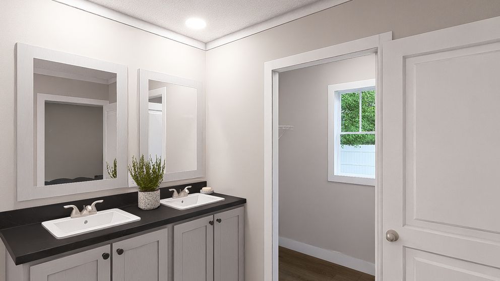 Bright bathroom vanity with double sinks, large mirror, and open doorway to a sunlit room.