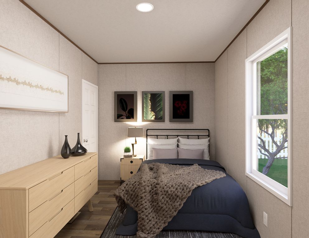 Small bedroom with beige walls, black bedspread, dresser, wall art, and a window showing greenery.