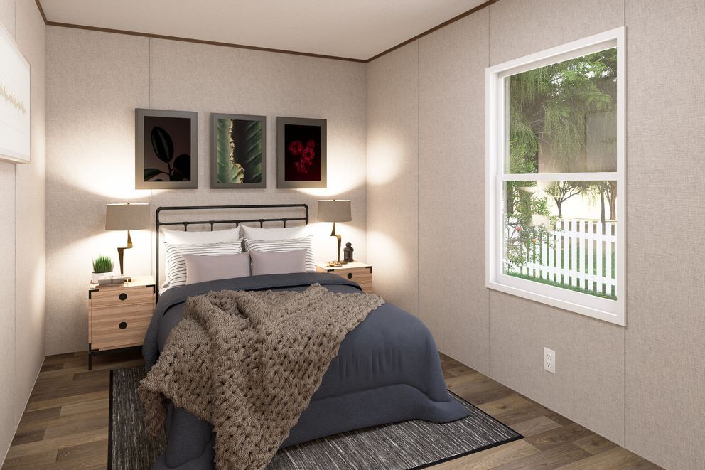 Small bedroom with a made bed, nightstands, wall art, and a window overlooking trees and a fence.