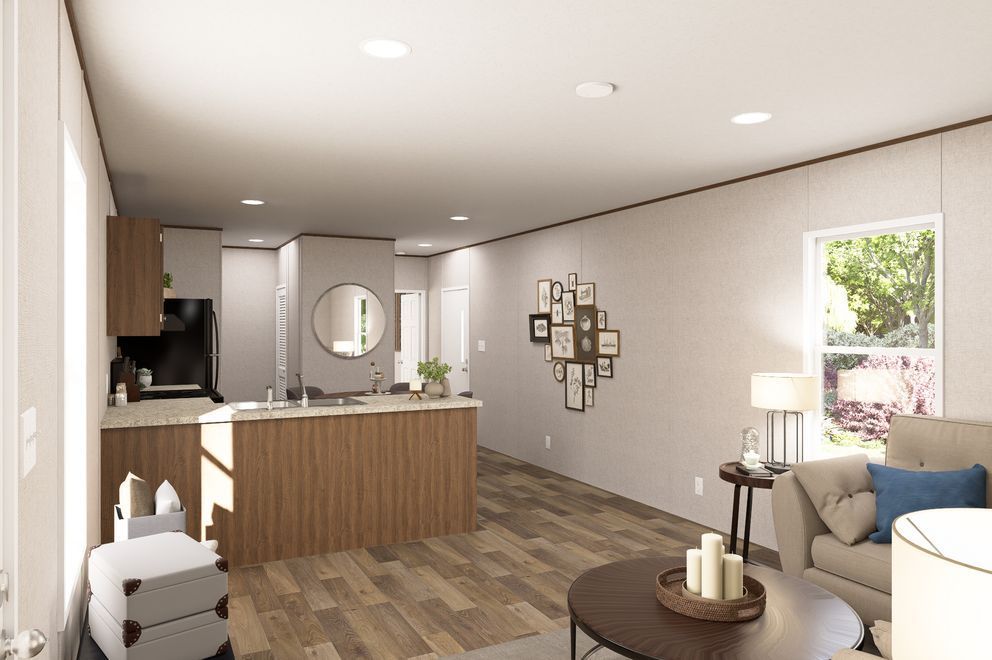 Modern open-plan living room and kitchen with wood floors, beige walls, gray sofa, and a window view.