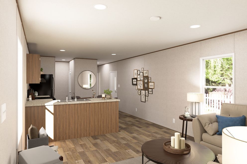 Modern open-plan living room and kitchen with wood cabinets, gray sofa, round table, and large window.