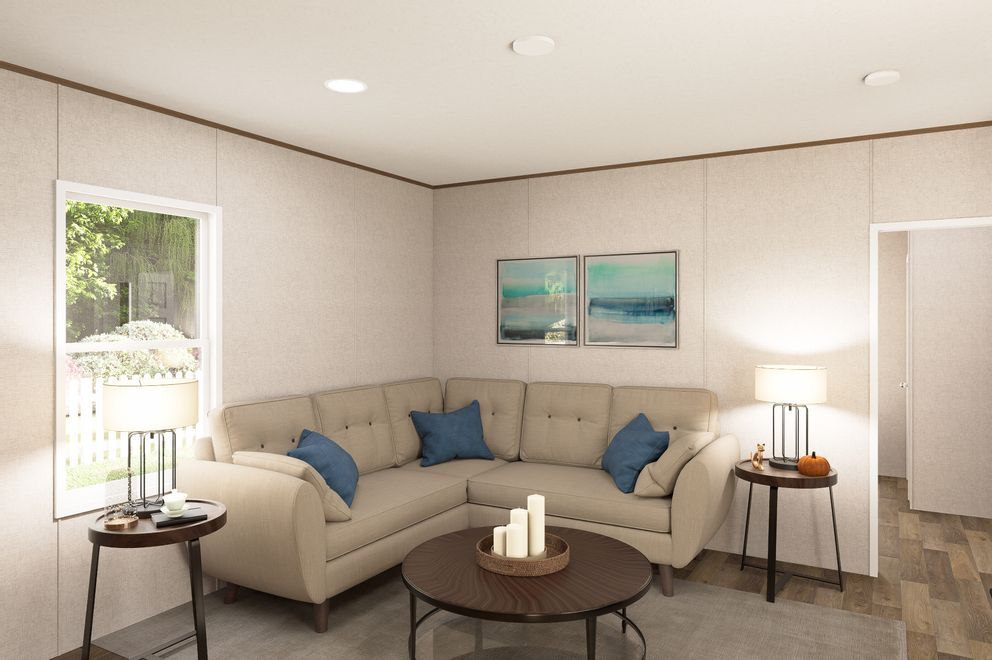 Bright beige living room with sectional sofa, blue pillows, round coffee table, and soft wall art, lit by a lamp