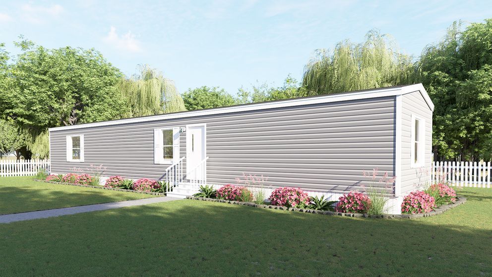 Single-story gray mobile home with white trim, small porch, and flower beds in a green yard