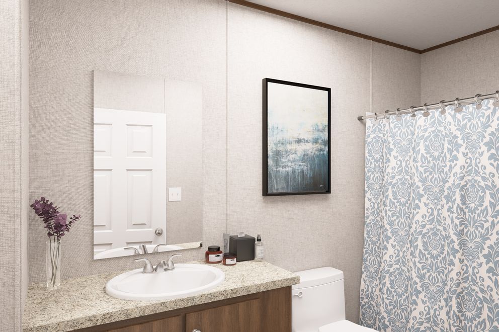 Bathroom vanity with sink, mirror, toilet, and blue patterned shower curtain.