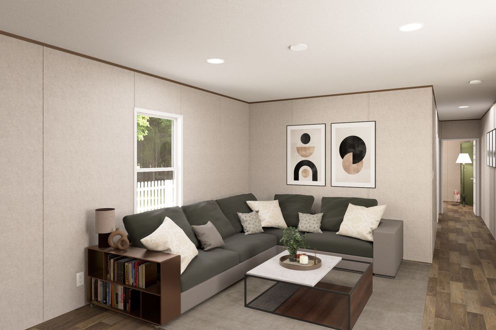 Modern living room with a gray sectional, coffee table, wall art, and bookshelves by a window.