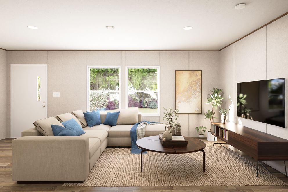 Bright modern living room with beige sofas, blue pillows, coffee table, and wall-mounted TV by a window.