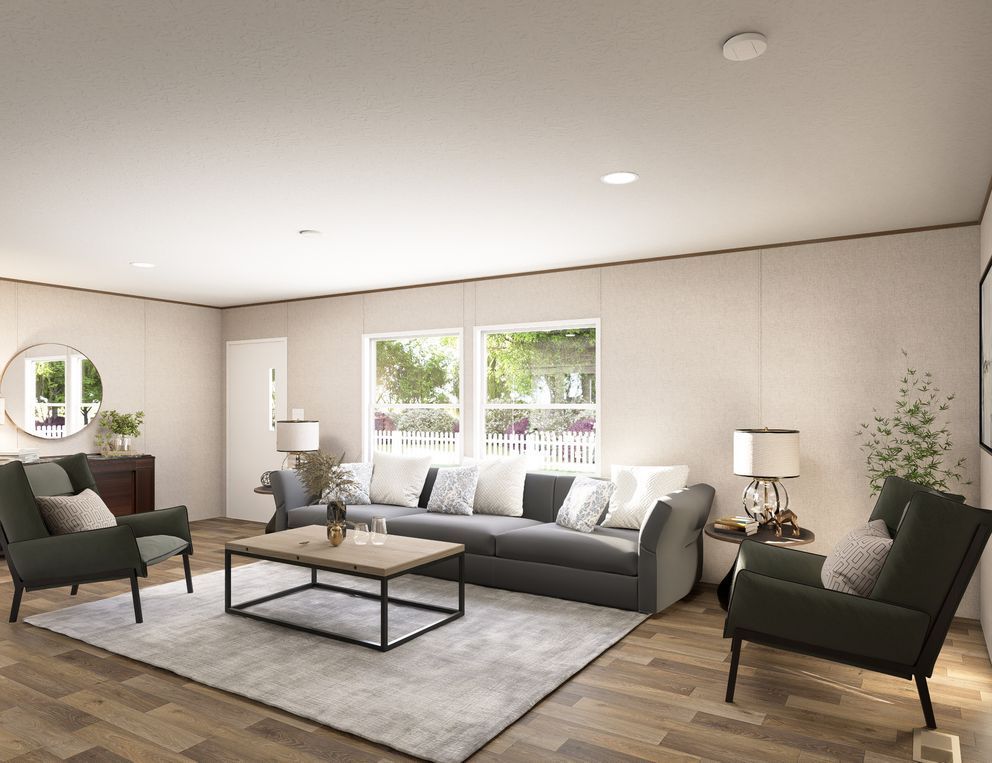 Bright modern living room with gray sofa, two green chairs, coffee table, rug, and large windows