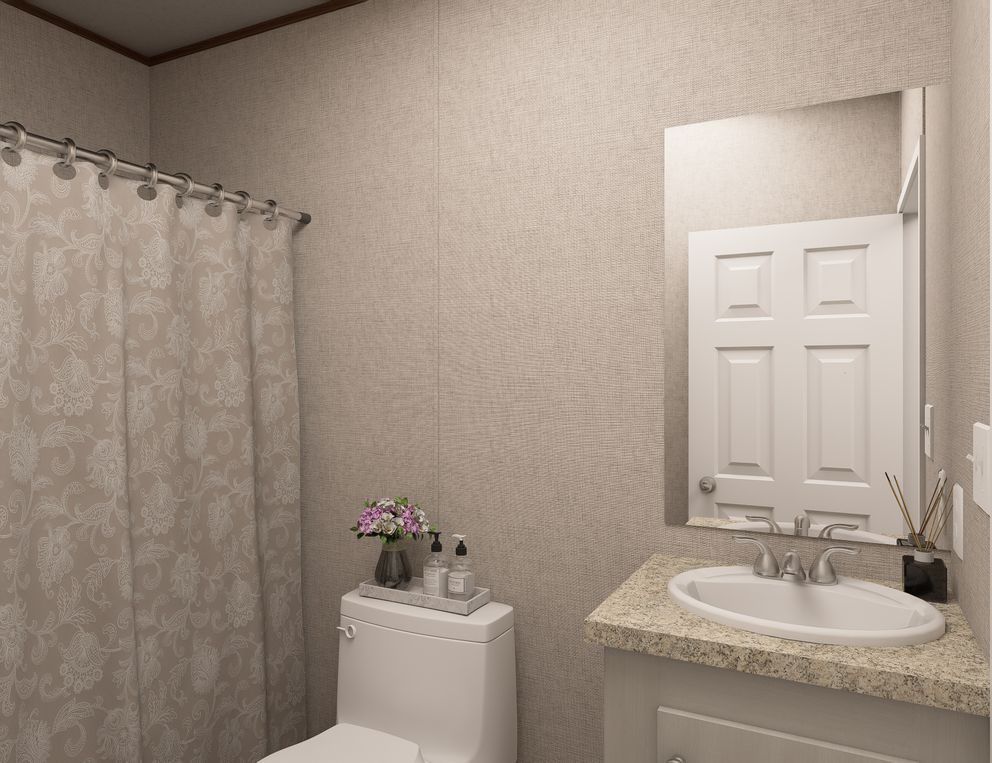 Small beige bathroom with shower curtain, vanity sink, mirror, and toilet decorated with flowers and bottles