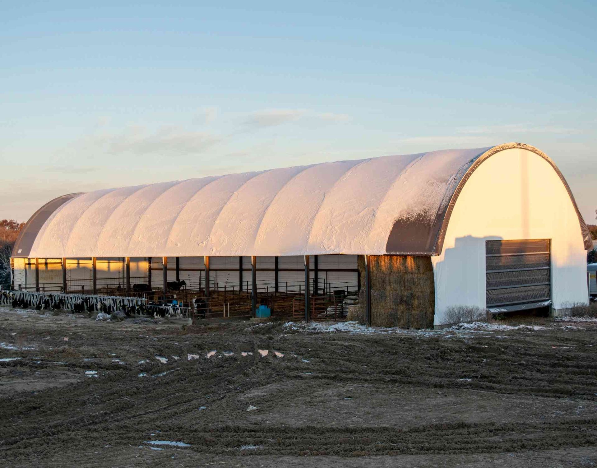 Snow-covered arched building with dark windows and wooden door, set in a rural, outdoor area.