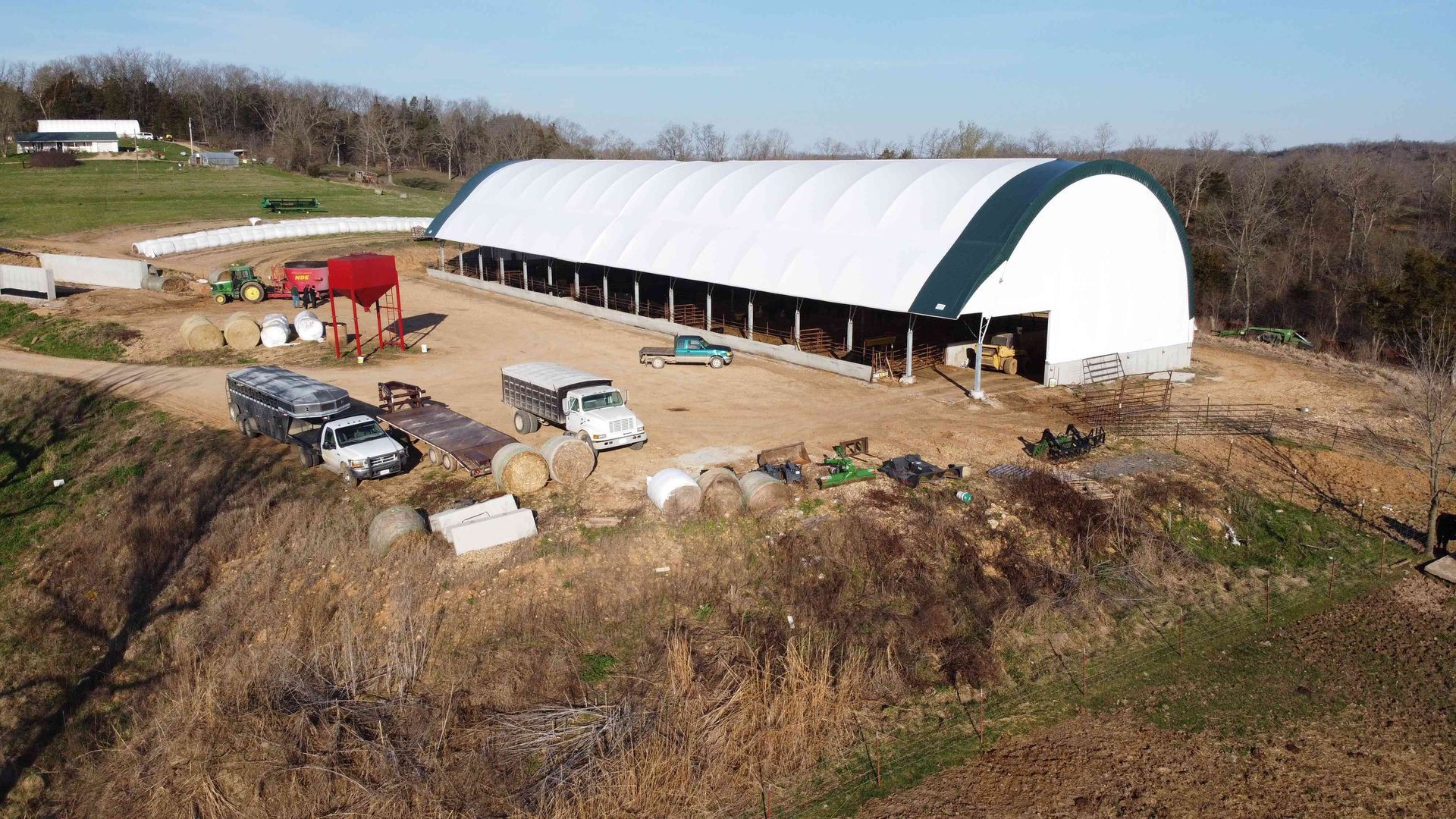 Aerial view of a farm with a large white barn and several trucks and equipment.