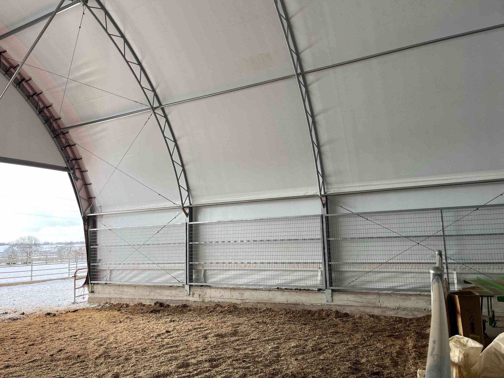 Interior of a large white arched-roof structure with dirt floor, open to snowy outdoor scene.