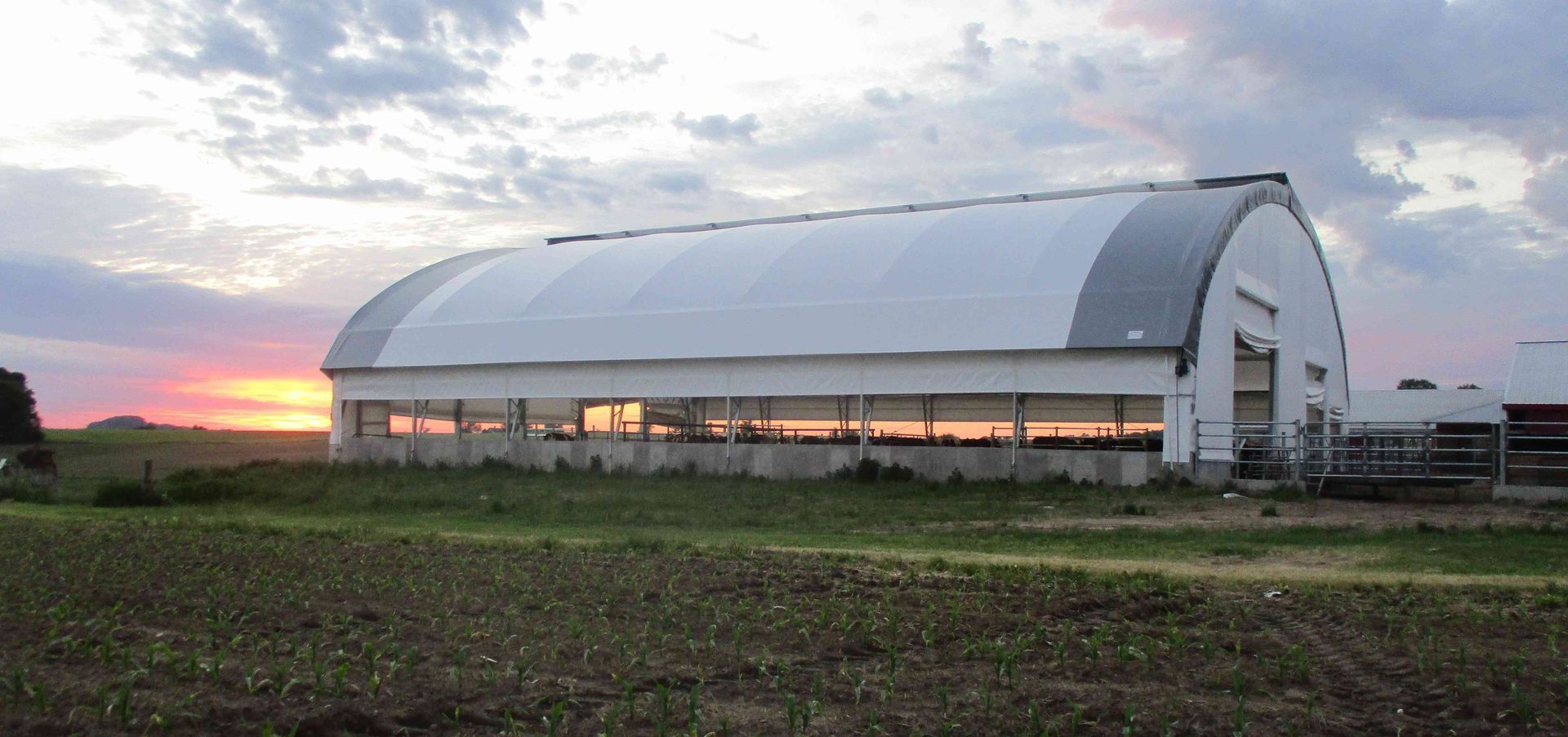 A large white building with a curved roof sits in a field at sunset.