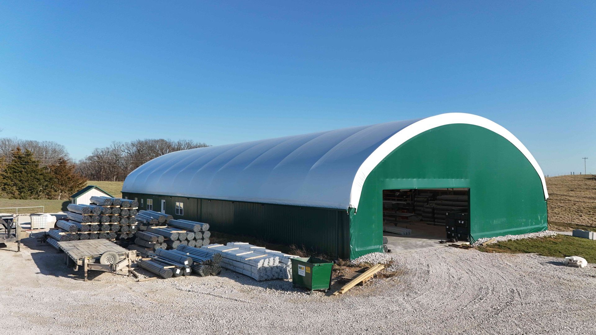 Green and white arched storage building with gravel ground.