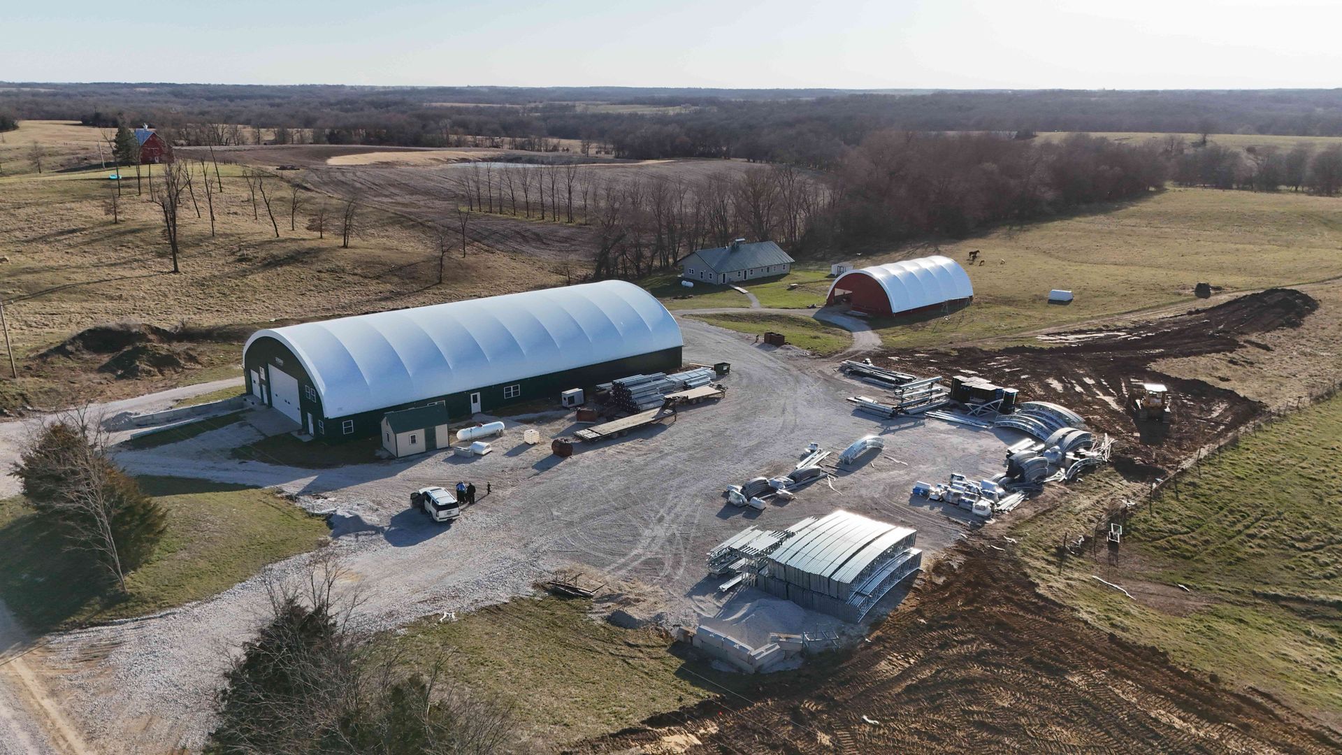Aerial view of a farm with two large white and red buildings. Construction materials are scattered around a gravel area.