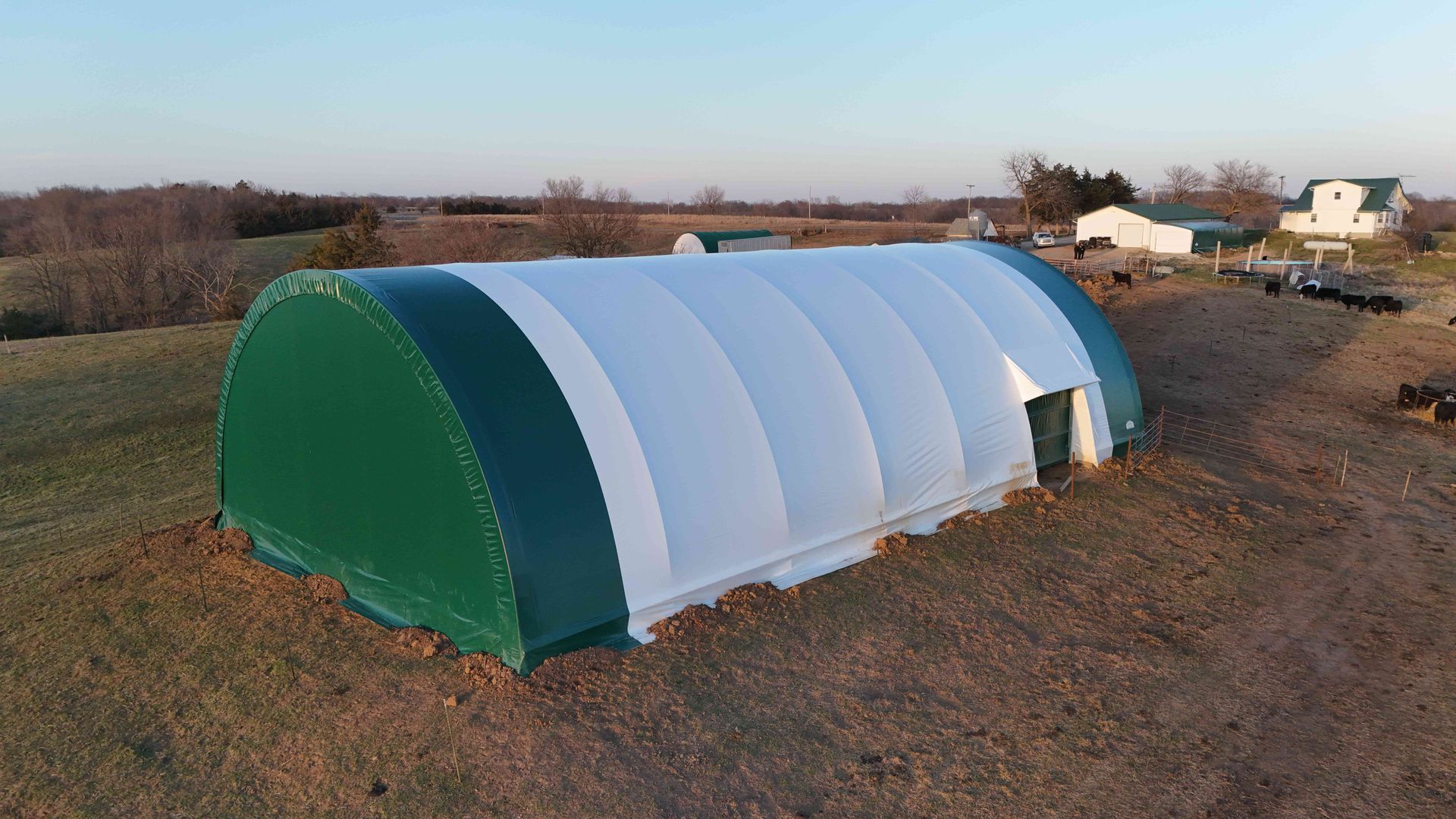 Green and white arched fabric structure in a rural field.